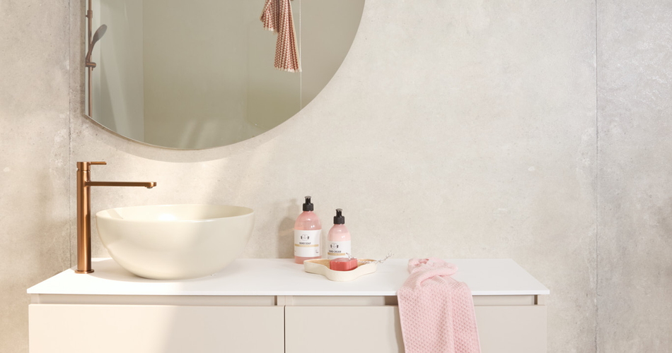 Badkamermeubel met halfronde spiegel in een rustige badkamer. Beige meubel met beige opzet waskom en bronskleurige wastafelkraan. In de reflectie van de spiegel zie je de douche.