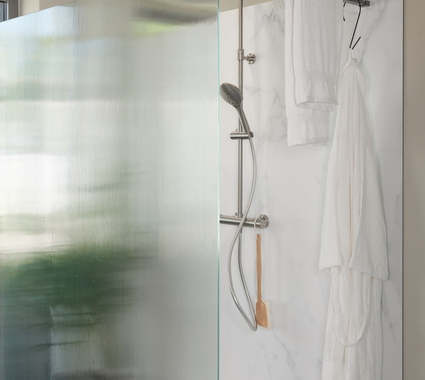 Inloopdouche met glazen wand van ribbelglas en marmerlook wandpaneel, voorzien van moderne douche en handdoekrek.