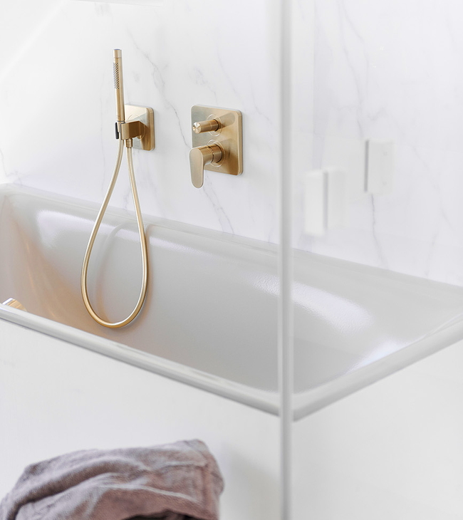 Inbouwbad met gouden badkraan en handdouche, afgewerkt met marmeren wandbekleding voor een luxe uitstraling.