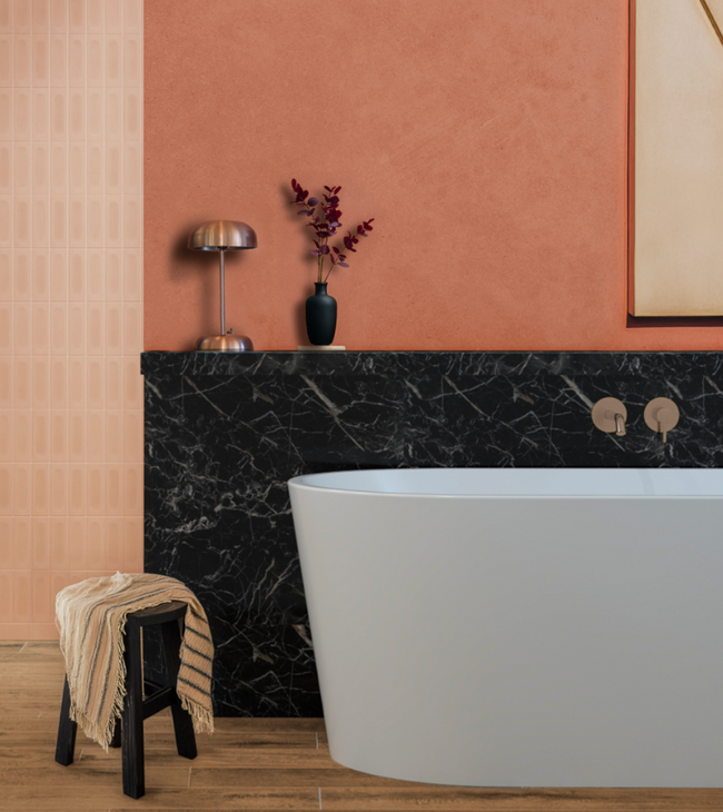 Vrijstaand bad met zwart marmeren achterwand, koperkleurige kraan en warme terracotta wand in stijlvolle badkamer.