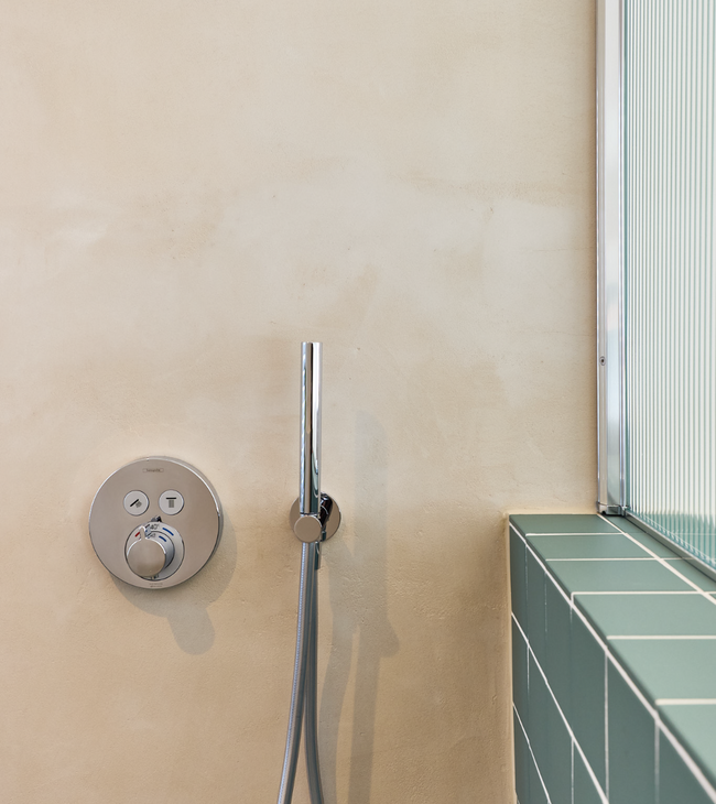 Halfhoge voorzetwand met groene tegels en ingebouwde douchekraan in een strakke, minimalistische badkamer.