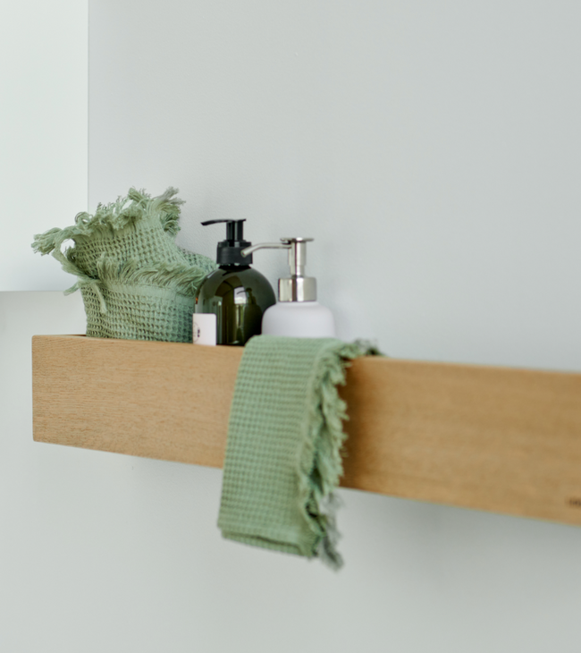Houten legplank in de badkamer met zeepdispensers, groen washandje en handdoek voor een natuurlijke, opgeruimde uitstraling.