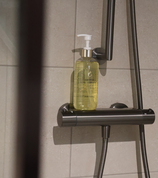 Douchekraan met gunmetal afwerking en douchegel, geplaatst tegen een betegelde wand voor eenvoudig onderhoud in de badkamer.