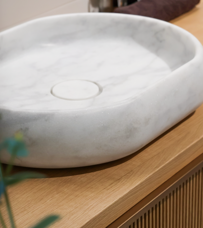 Opzetwaskom in carrara marmer op houten badkamermeubel, met natuurlijke uitstraling passend in een biophilic design badkamer.
