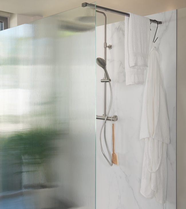 Inloopdouche met glazen wand van ribbelglas en marmerlook wandpaneel, voorzien van moderne douche en handdoekrek.