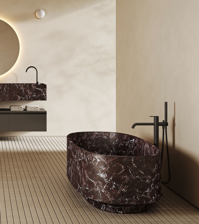 Luxe badkamer met vrijstaand rood marmeren bad en bijpassende marmeren wastafel tegen een beige wand en vloer.