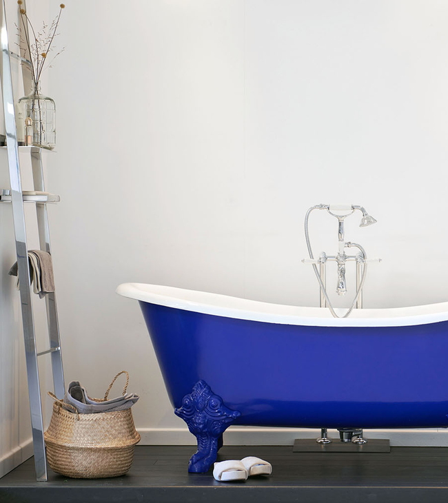 Bad op poten in opvallend blauw met sierlijke details, gecombineerd met klassieke kraan en ladderrek voor een stijlvolle badkamer.