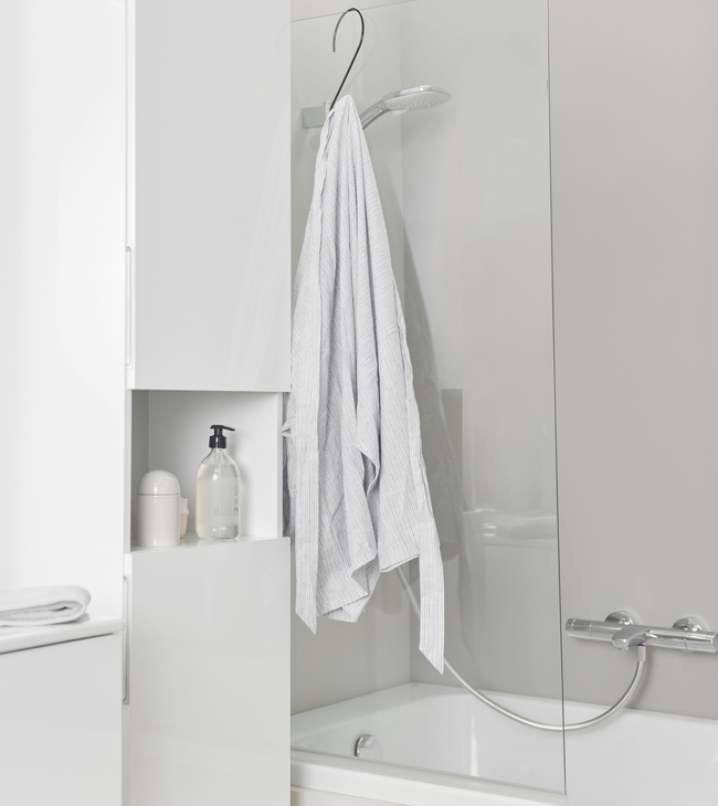 Wit bad met glazen badscherm en chromen kraan, naast witte kast en accessoires voor een frisse, moderne badkamerlook.