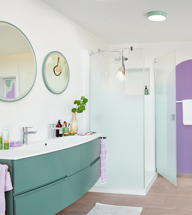 Moderne badkamer met mat glas douchecabine, groen badmeubel en ronde spiegels in frisse pastelkleuren.