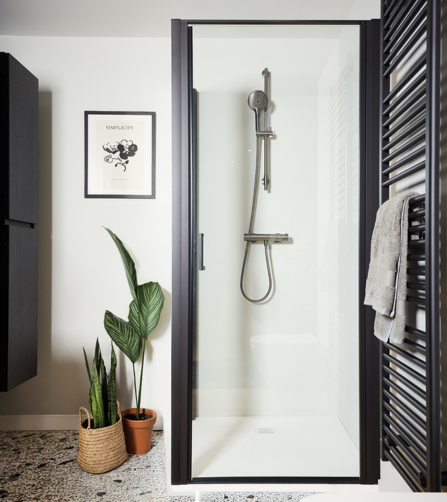 Moderne badkamer met douchedeur in zwart frame, terrazzo vloer en zwarte handdoekradiator naast de douche.