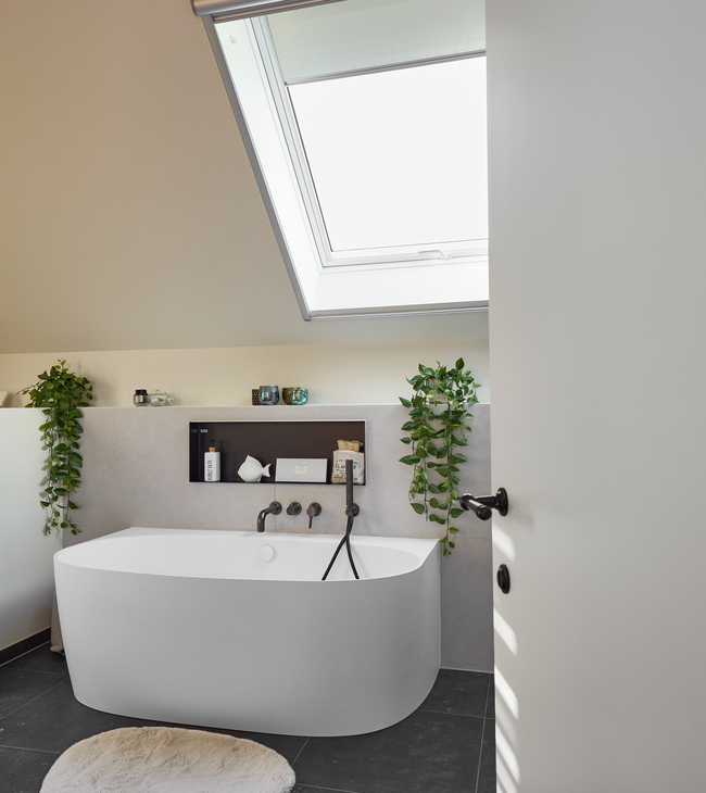 Moderne badkamerrenovatie met back-to-wall bad onder een dakraam, zwarte accenten en groene planten voor een frisse uitstraling.