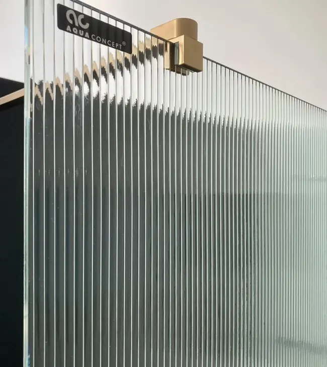Detail van een douchewand met geribbeld glas en een goudkleurige muurbevestiging van Aquaconcept.