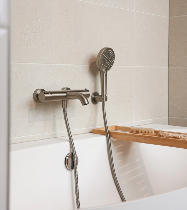 Nette afwerking van badkraan en handdouche door loodgieter, geplaatst tegen beige wandtegels met houten badplank.