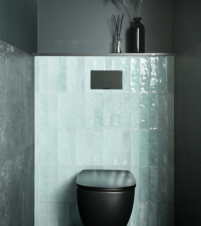 Modern toilet met zwarte pot, groene tegels op de achterwand en donkere muren voor een stijlvol contrast.