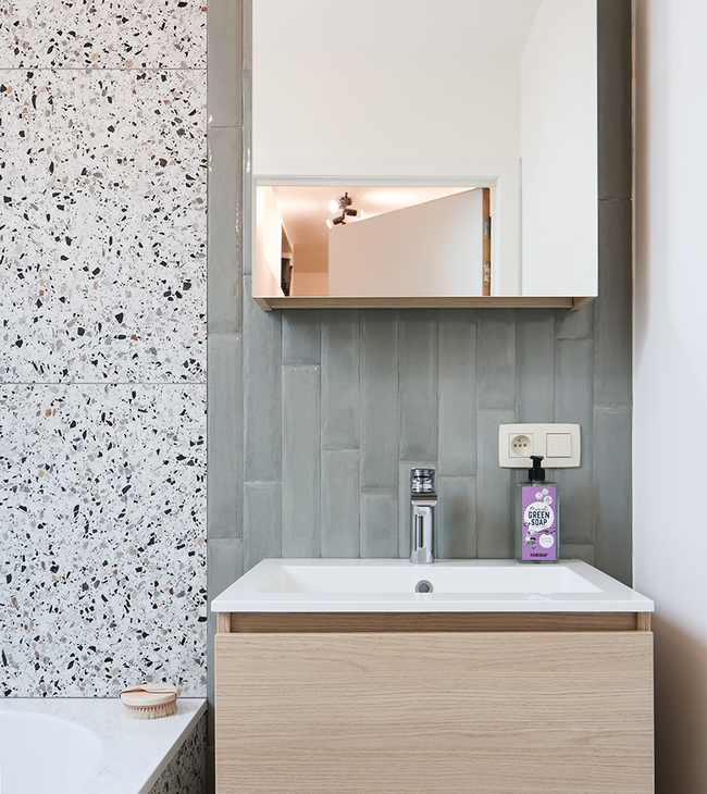Compact badkamermeubel met wastafel, spiegelkast en wand met groene langwerpige tegels naast terrazzo badombouw.