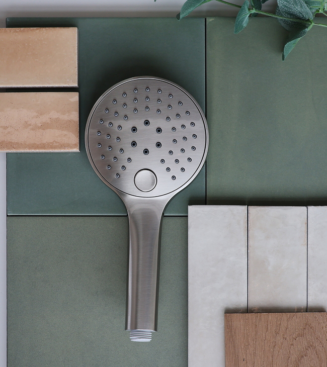 Moodboard met groene en beige tegels, houten accent en rvs handdouche, gecombineerd met een tak groene bladeren.