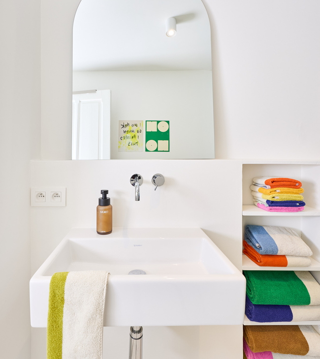 Vrijhangende wastafel met inbouwkraan, kleurrijke handdoeken in nis en grote spiegel in moderne badkamer.