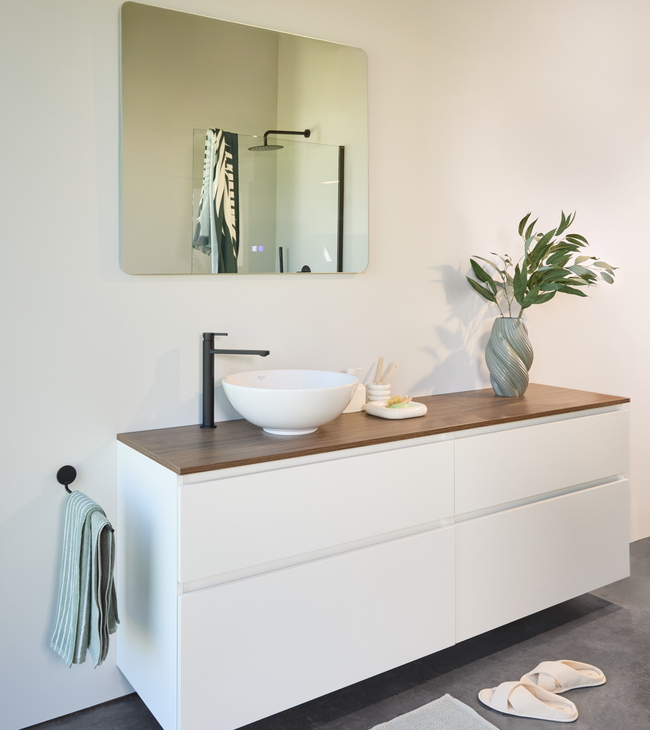 Nordic badkamerinterieur met wit gelakt meubel, houten blad, opbouwkom, zwarte kraan en ronde spiegel.