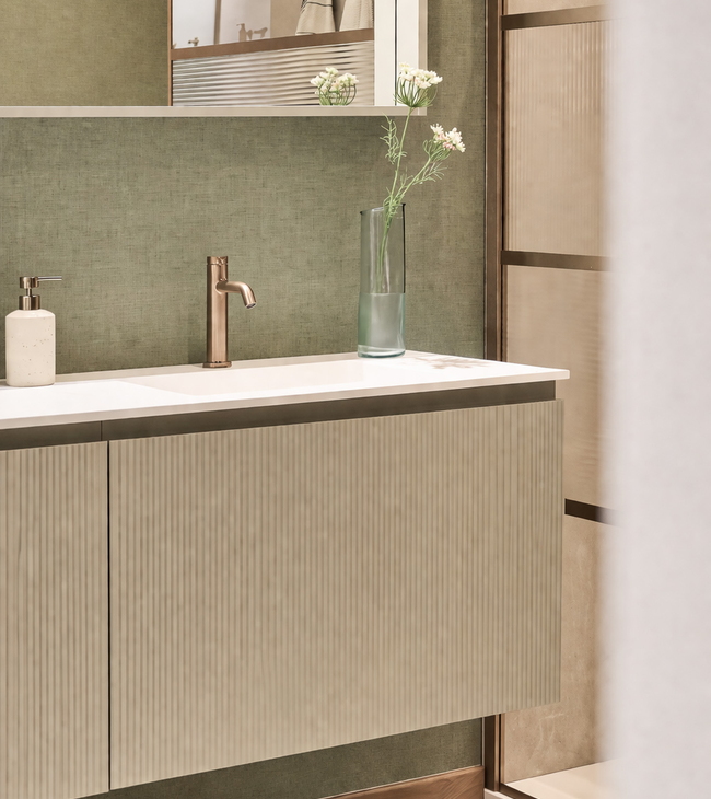 Badkamer met saliegroen badkamermeubel met brons kraanwerk en een douche geribbeld glas en bronskleurige profielen op een saliegroene muur