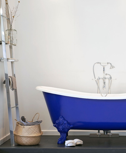 Bad op poten in opvallend blauw met sierlijke details, gecombineerd met klassieke kraan en ladderrek voor een stijlvolle badkamer.