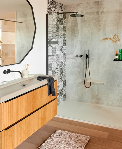 Badkamer met wandpaneel in betonlook en zwart-wit patroon, gecombineerd met zwarte regendouche en houten wastafelmeubel.