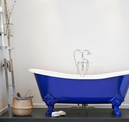 Bad op poten in opvallend blauw met sierlijke details, gecombineerd met klassieke kraan en ladderrek voor een stijlvolle badkamer.