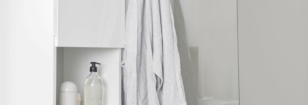 Wit bad met glazen badscherm en chromen kraan, naast witte kast en accessoires voor een frisse, moderne badkamerlook.