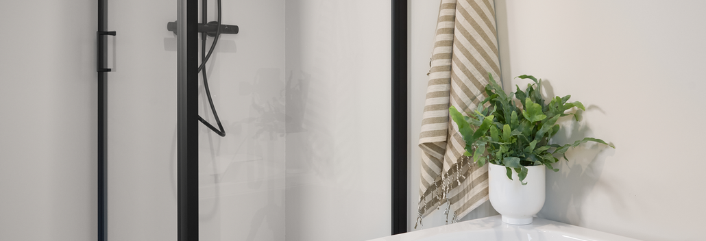 Moderne douche met zwarte profielen naast een wit bad, ingericht met planten en accessoires voor een strakke badkamerstijl.