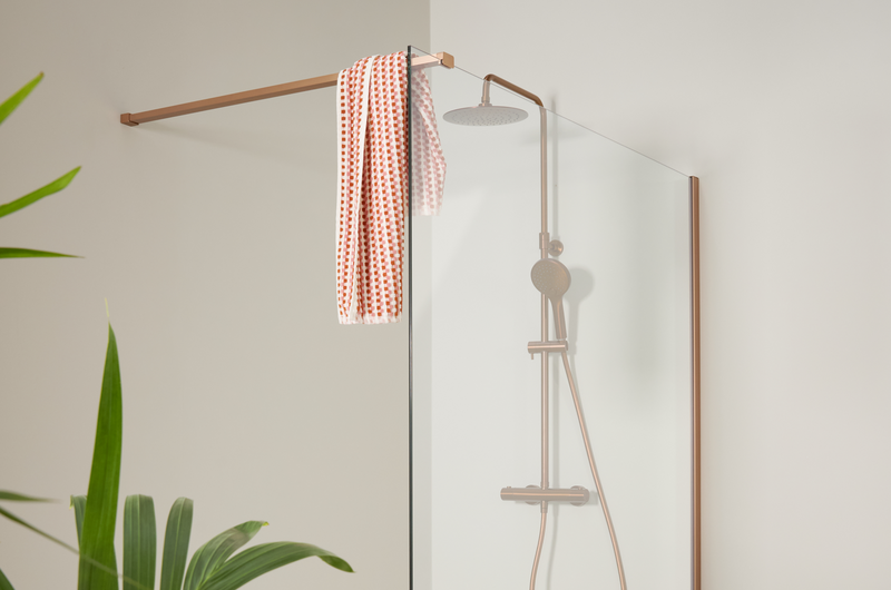 Moderne inloopdouche met brushed copper douchekraan en glazen wand, gecombineerd met lichte muren en groene plant.